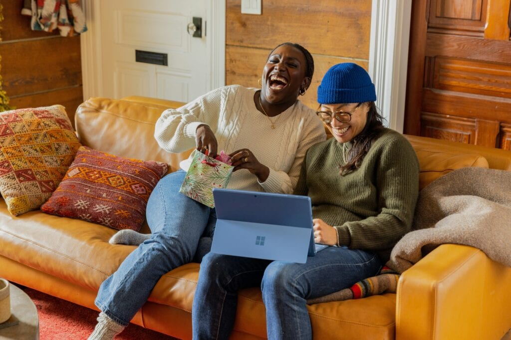 two people sitting on a couch working on a laptop and laughing